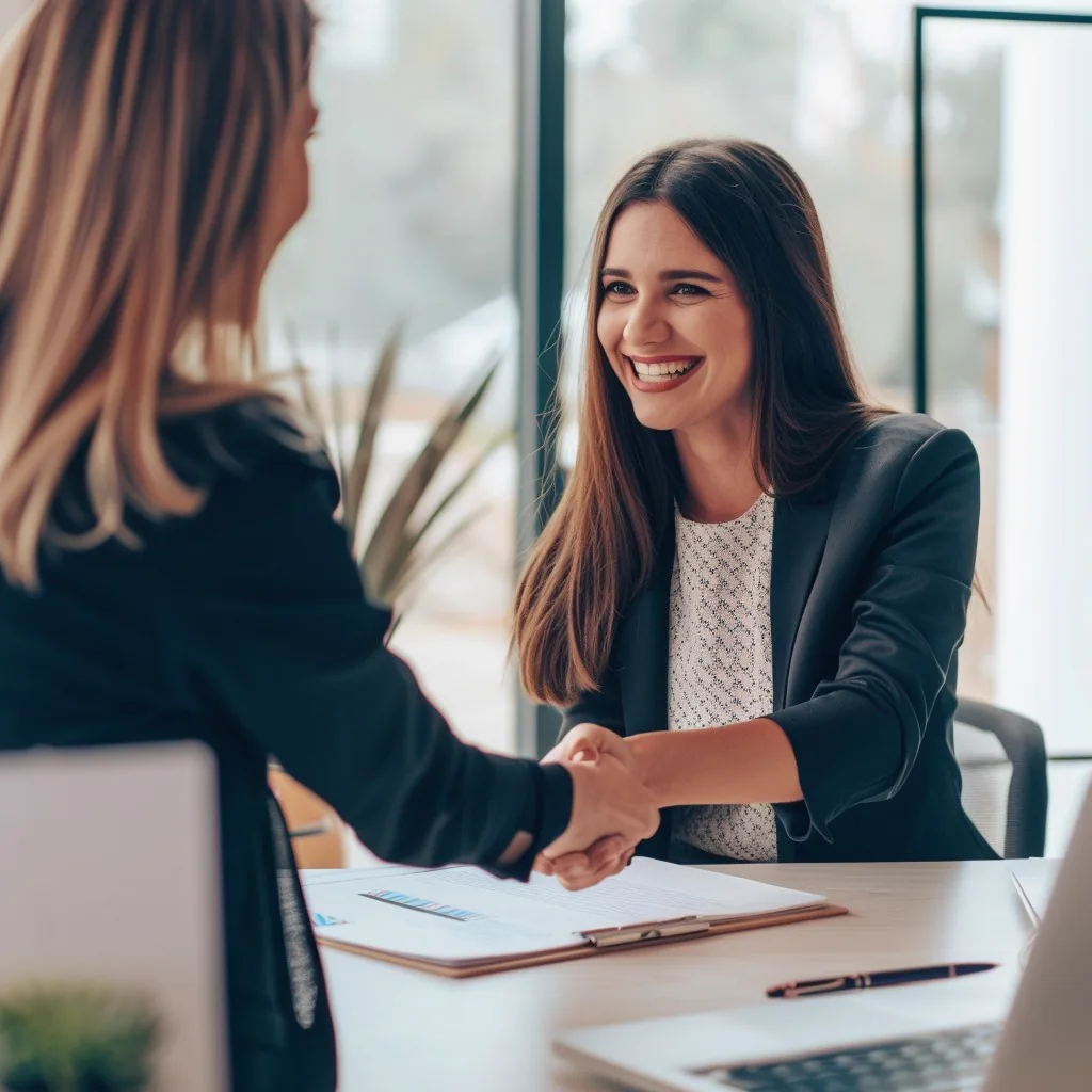Business partners shaking hands across a table while reviewing insurance documents